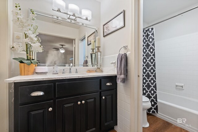 full bathroom featuring hardwood / wood-style floors, shower / bath combo with shower curtain, toilet, vanity, and ceiling fan