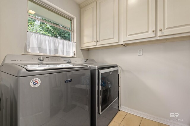 clothes washing area featuring cabinets, light tile patterned floors, and washing machine and clothes dryer