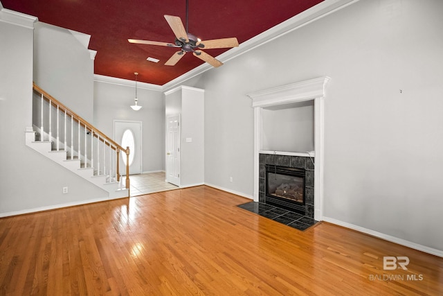 unfurnished living room featuring ornamental molding, wood finished floors, baseboards, ceiling fan, and a tiled fireplace