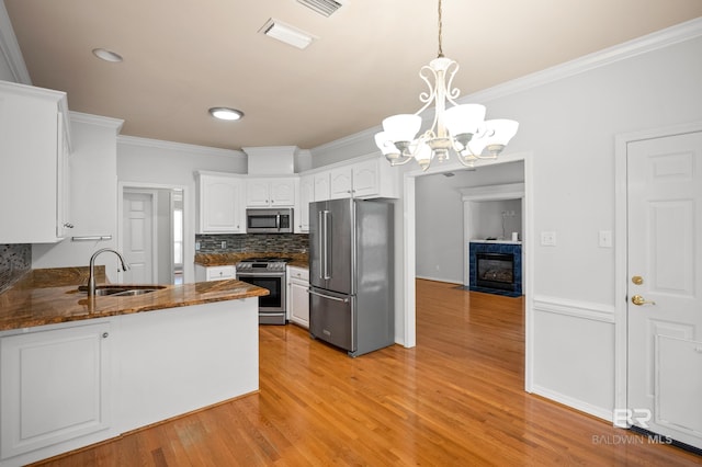kitchen featuring an inviting chandelier, a sink, stainless steel appliances, a peninsula, and ornamental molding