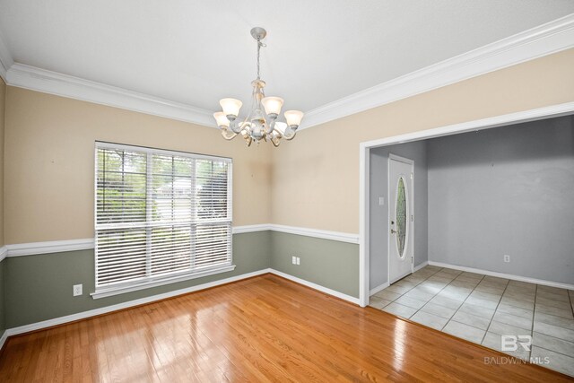 spare room with baseboards, ornamental molding, wood finished floors, and a notable chandelier