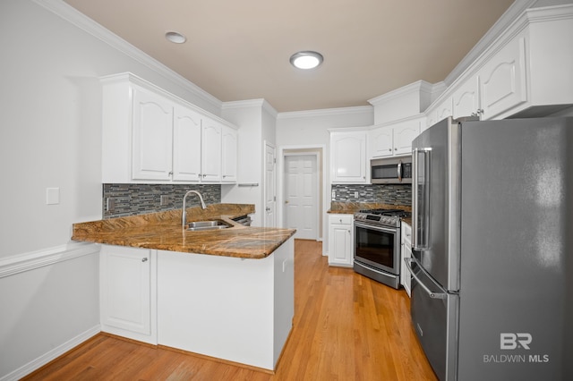 kitchen featuring decorative backsplash, appliances with stainless steel finishes, a sink, a peninsula, and white cabinetry