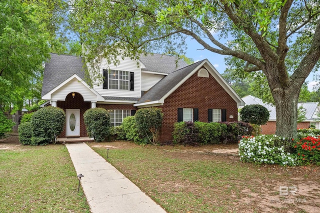 traditional home with a shingled roof, a front yard, and brick siding