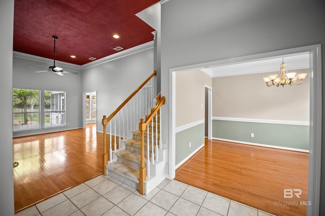 staircase with visible vents, tile patterned floors, baseboards, ceiling fan with notable chandelier, and ornamental molding