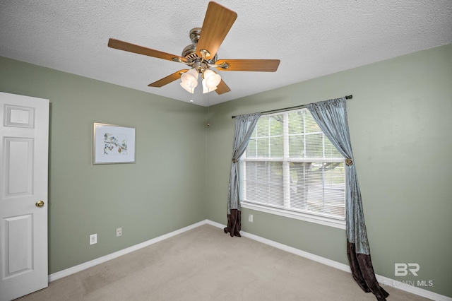 spare room featuring light colored carpet, a textured ceiling, ceiling fan, and baseboards