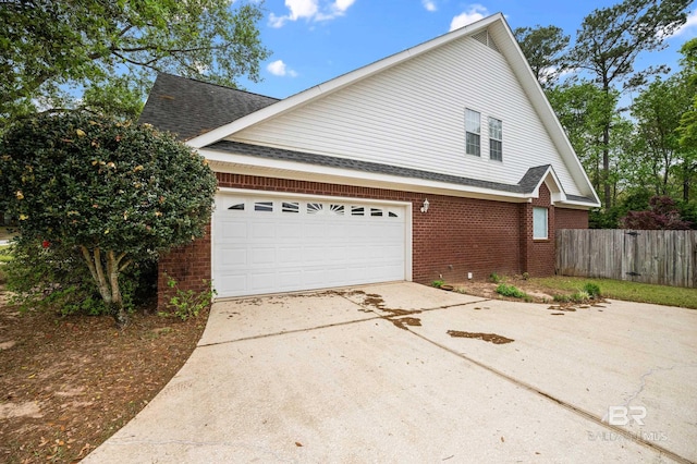view of side of property with fence, roof with shingles, brick siding, concrete driveway, and an attached garage