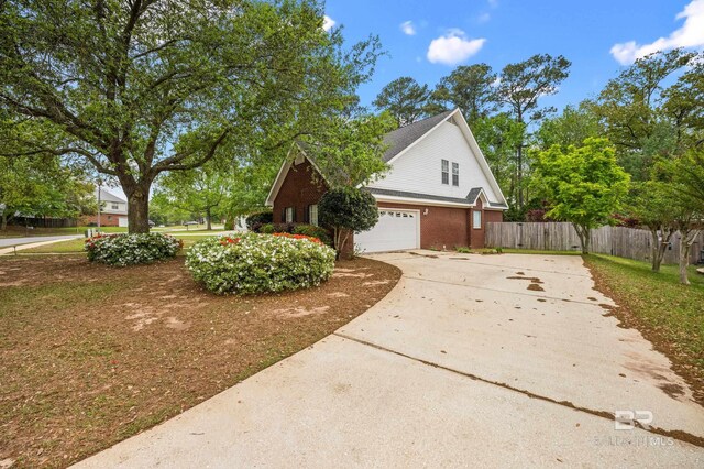 view of side of property with fence, an attached garage, concrete driveway, and brick siding
