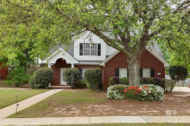 view of front of property with brick siding, fence, roof with shingles, and a front lawn