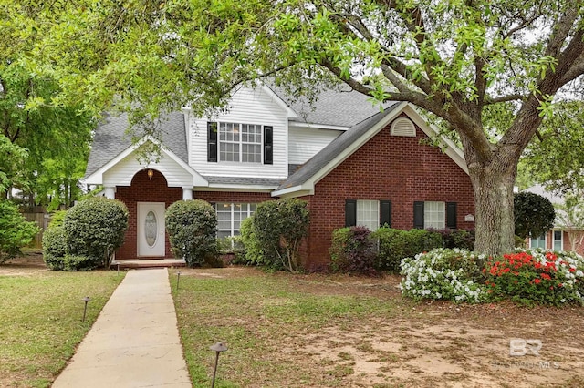 traditional home with roof with shingles, a front yard, and brick siding