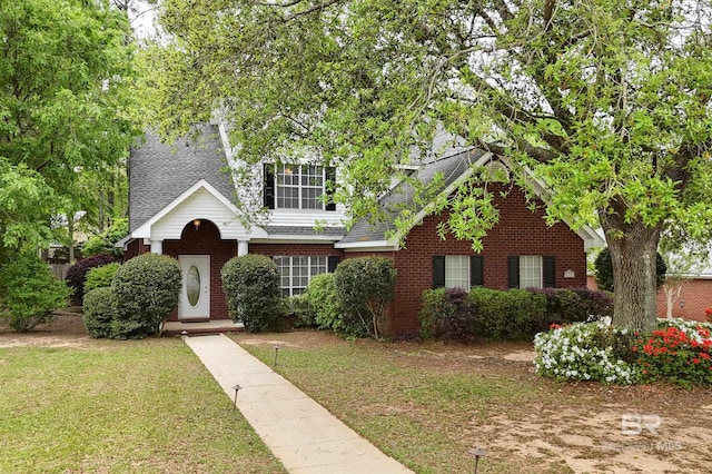 view of front of home featuring a shingled roof, brick siding, and a front yard