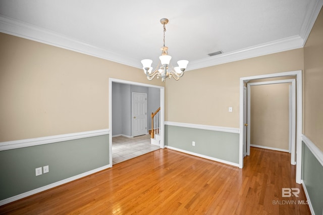 spare room featuring crown molding, wood finished floors, a chandelier, and visible vents