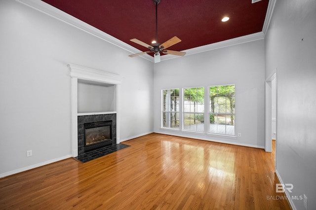 unfurnished living room with crown molding, a tiled fireplace, a ceiling fan, baseboards, and wood finished floors