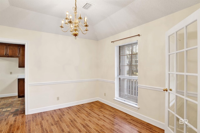 unfurnished dining area featuring hardwood / wood-style flooring, lofted ceiling, and a notable chandelier