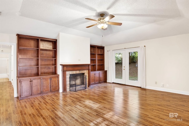 unfurnished living room featuring french doors, a raised ceiling, ceiling fan, and a brick fireplace