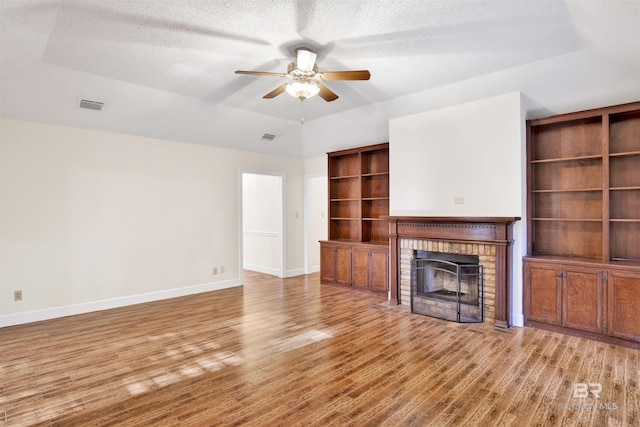 unfurnished living room with a fireplace, a textured ceiling, a tray ceiling, and ceiling fan