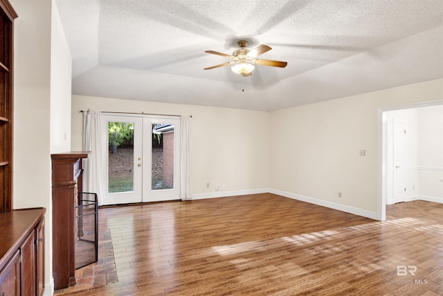 unfurnished living room featuring ceiling fan, french doors, a textured ceiling, vaulted ceiling, and hardwood / wood-style flooring