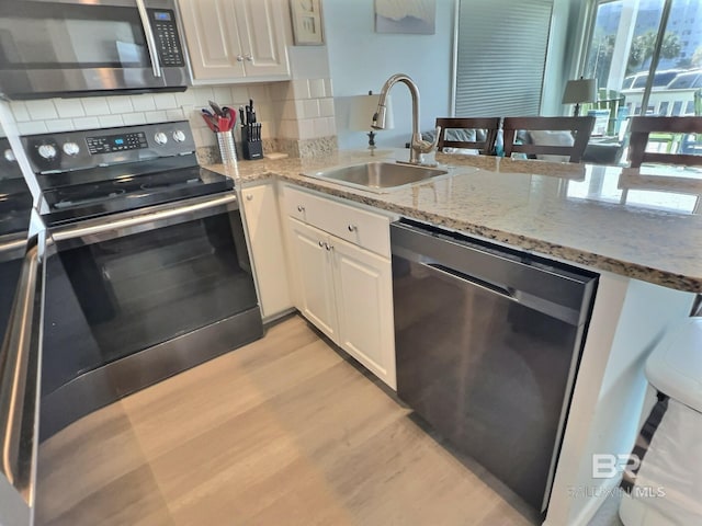 kitchen featuring sink, stainless steel appliances, light stone counters, white cabinets, and decorative backsplash