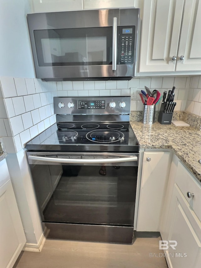 kitchen with stainless steel appliances, light stone countertops, white cabinets, and backsplash