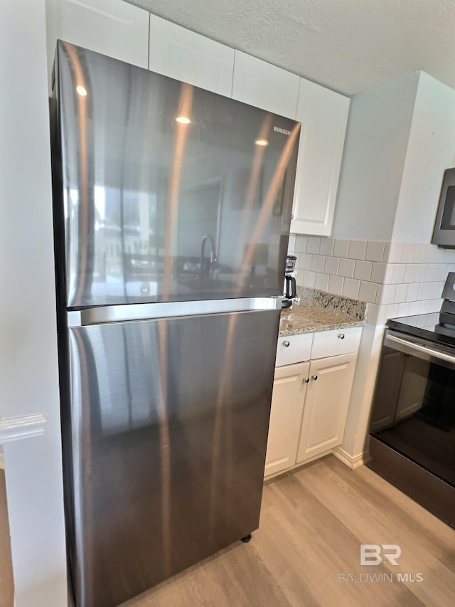 kitchen with white cabinetry, decorative backsplash, stainless steel appliances, and light wood-type flooring