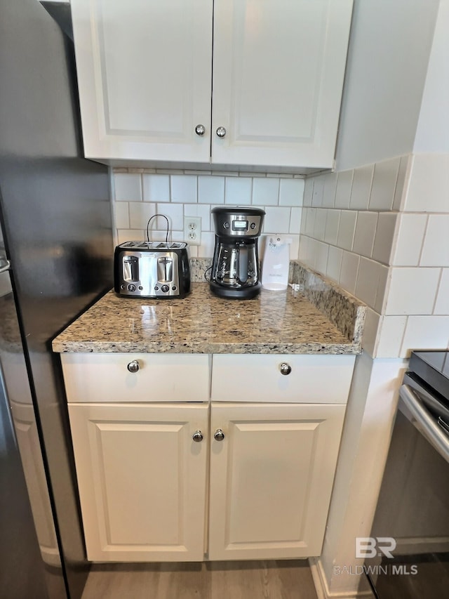 kitchen featuring white cabinetry, black refrigerator, backsplash, and light stone counters