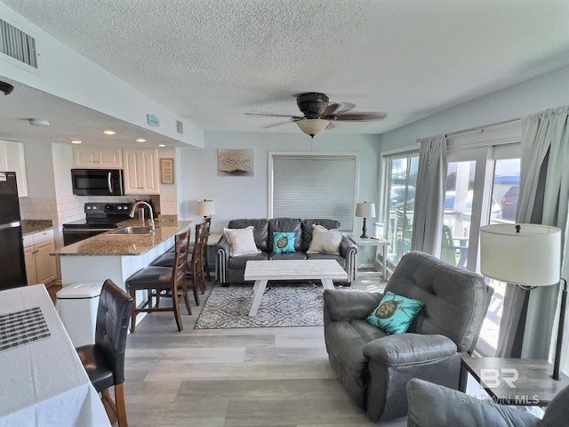 living room with ceiling fan, sink, a textured ceiling, and light hardwood / wood-style flooring