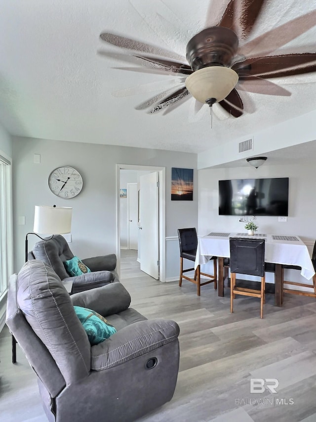 living room with ceiling fan, light hardwood / wood-style flooring, and a textured ceiling