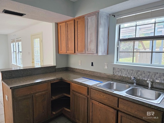 kitchen with kitchen peninsula, dark tile patterned flooring, a healthy amount of sunlight, and sink