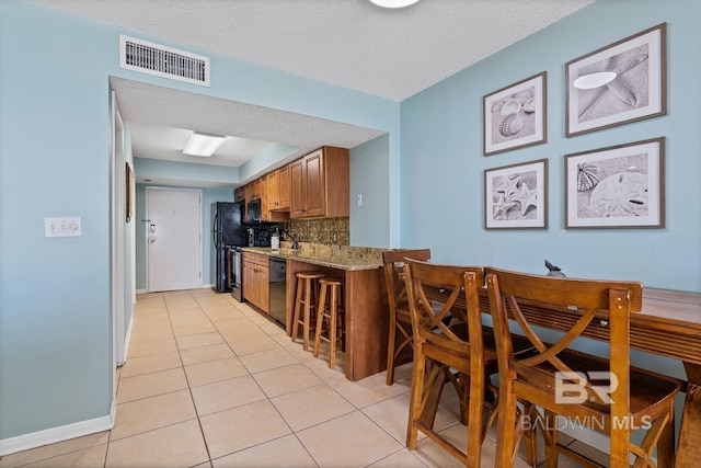 kitchen with light stone countertops, visible vents, decorative backsplash, black appliances, and brown cabinets