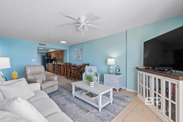 living room featuring light tile patterned floors, a ceiling fan, visible vents, and a textured ceiling