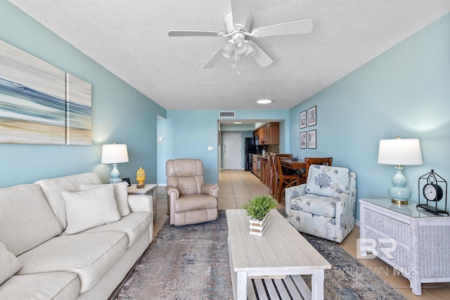 living area with light tile patterned floors, visible vents, a textured ceiling, and ceiling fan