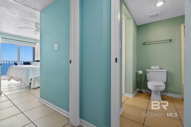 ensuite bathroom with tile patterned floors, visible vents, toilet, a textured ceiling, and baseboards