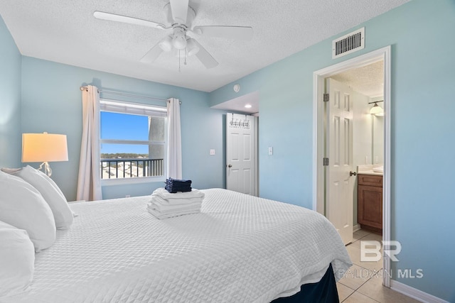 bedroom with visible vents, baseboards, light tile patterned floors, ensuite bath, and a textured ceiling