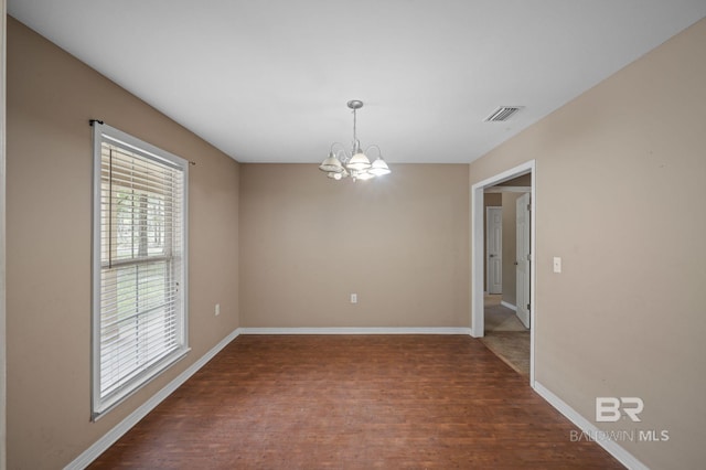 spare room with a chandelier, wood finished floors, and baseboards