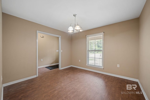 spare room with dark wood-style flooring, a chandelier, and baseboards