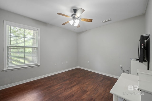 empty room with dark wood-style floors, a ceiling fan, and baseboards