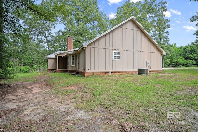 view of home's exterior featuring board and batten siding, a chimney, central AC unit, and a yard