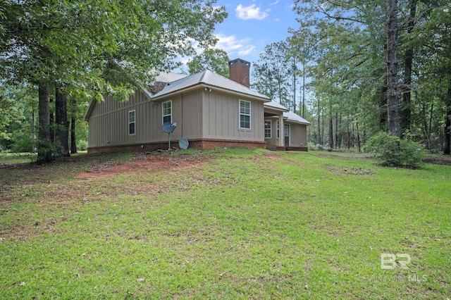 back of property featuring a chimney, board and batten siding, a yard, and metal roof