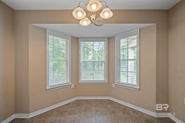 tiled spare room with a chandelier and baseboards