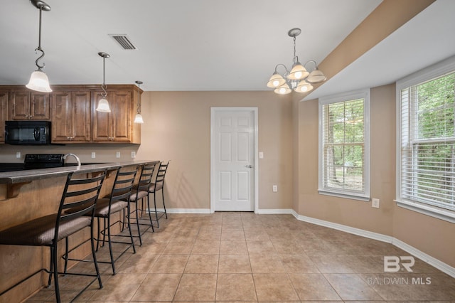 kitchen featuring black appliances, a breakfast bar, light tile patterned floors, a chandelier, and hanging light fixtures