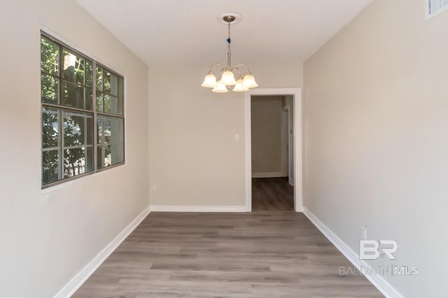 unfurnished dining area with baseboards, wood finished floors, visible vents, and an inviting chandelier