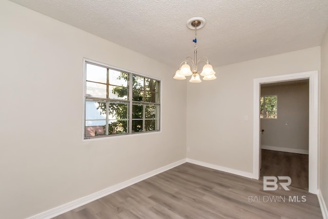 spare room featuring a textured ceiling, a notable chandelier, wood finished floors, and baseboards