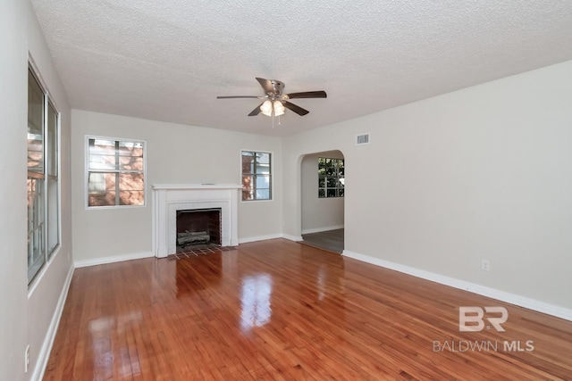 unfurnished living room featuring visible vents, arched walkways, a ceiling fan, wood-type flooring, and a fireplace with flush hearth