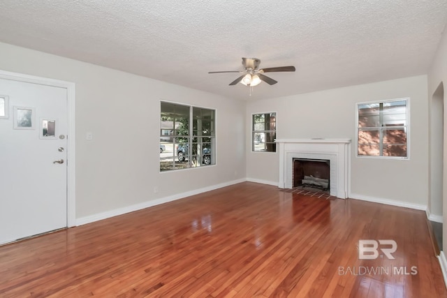 unfurnished living room featuring a brick fireplace, a textured ceiling, a ceiling fan, and wood finished floors