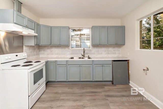 kitchen with white electric stove, light countertops, backsplash, a sink, and under cabinet range hood