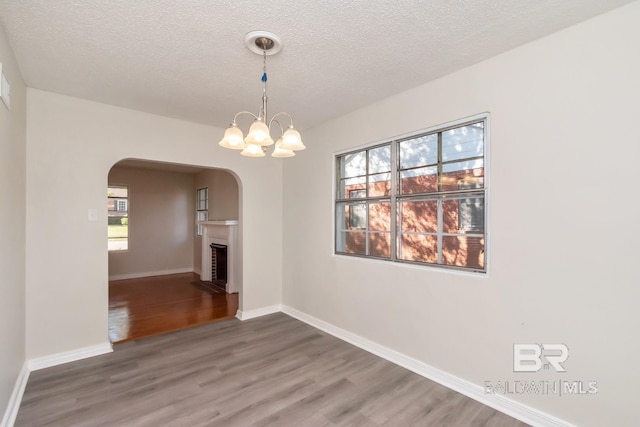 unfurnished dining area with baseboards, arched walkways, a fireplace with flush hearth, wood finished floors, and a textured ceiling