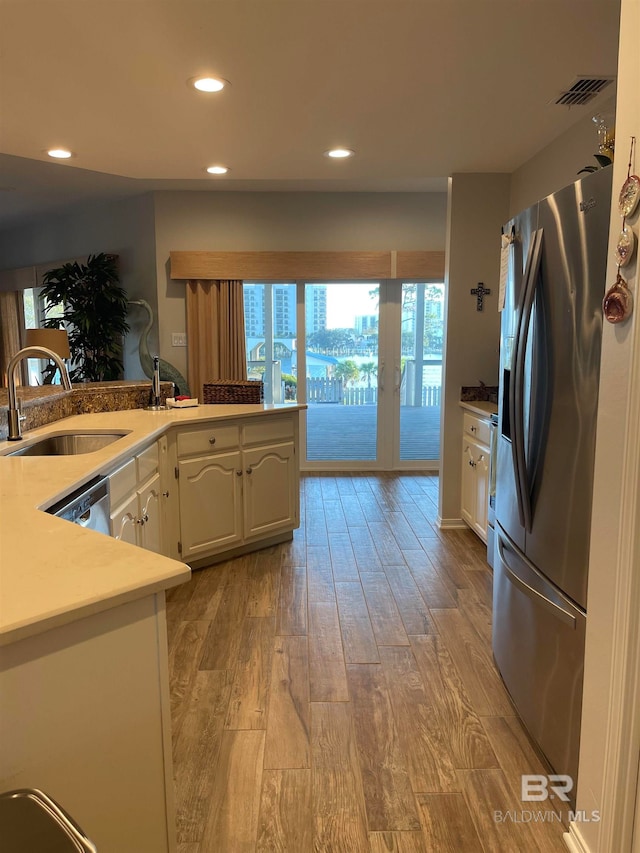 kitchen with sink, kitchen peninsula, light hardwood / wood-style floors, stainless steel appliances, and white cabinets