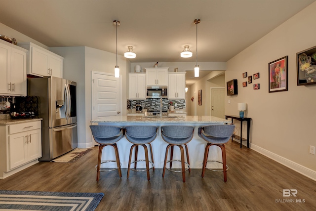 kitchen with stainless steel appliances, tasteful backsplash, pendant lighting, a center island with sink, and white cabinets