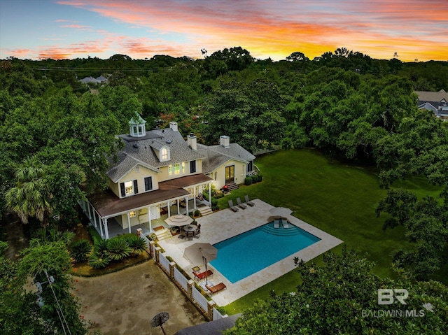 back house at dusk featuring a lawn and a patio