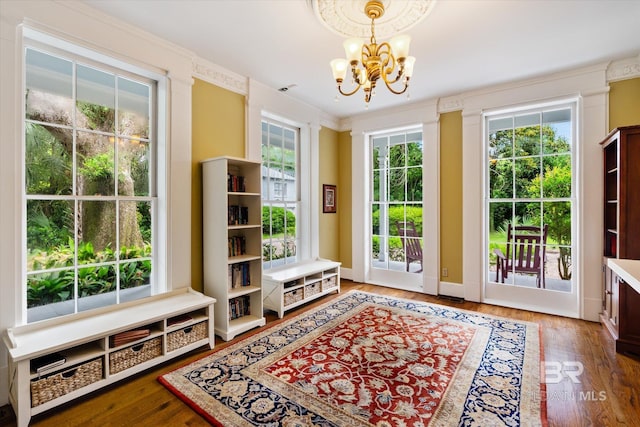 doorway to outside with wood-type flooring, crown molding, and an inviting chandelier