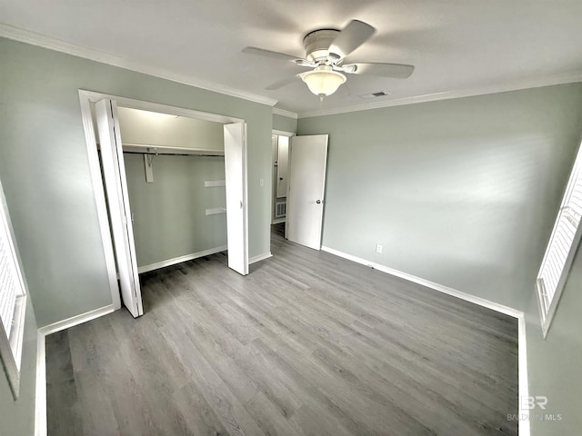 unfurnished bedroom with wood finished floors, visible vents, baseboards, a closet, and crown molding